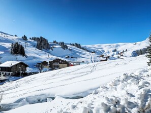 A snow-covered mountain village with traditional wooden buildings, ski slopes, and a clear blue sky.