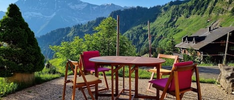 Une table et des chaises en bois sont disposées à l’extérieur, offrant une vue sur la montagne.