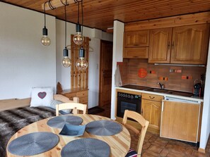 A cozy kitchen with wooden cabinets, a dining table with woven placemats, and pendant lights. - Résid. Les Lupins, (Les Crosets), by Interhome (Les Crosets)