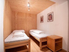 A small, wooden room with two single beds, a wooden nightstand, and two framed pictures on the wall.
