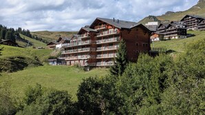 A multi-story hotel with balconies, set in a mountainous area with green hills and trees. - Sundance 5, (Les Crosets), by Interhome (Les Crosets)