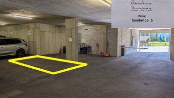 Eine Parkgarage mit einem weißen Auto, das in einem markierten Stellplatz geparkt ist. Ein Schild zeigt 'Privé Sundance 5' und ein gelb umrandeter Bereich ist auf dem Boden zu sehen.