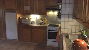 A kitchen with wooden cabinets, a white refrigerator, a microwave, a toaster, a stove, and a sink with a dish rack. - Chalet Carmazin, (Morgins), by Interhome (Morgins)