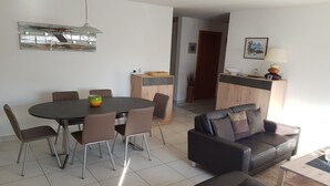 Ein modernes Wohnzimmer mit einem runden Esstisch, einer Ledersofa und einer Küchenzeile im Hintergrund.