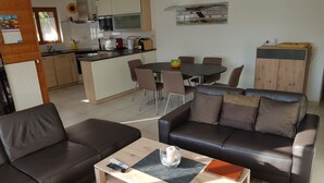 Ein modernes Wohnzimmer mit einem braunen Ledersofa, einem Holztisch und einem Essbereich mit rundem Tisch und Stühlen.