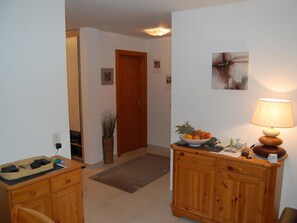 A hallway with a wooden cabinet, a bowl of fruit, a lamp, and a door. - Résid. Mila 5, (Champery), by Interhome (Champery)