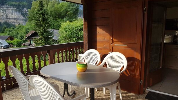 Ein Balkon mit Tisch und Stühlen, eine Holztür und Blick auf einen Berg sowie Häuser.