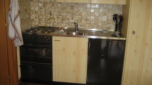 Eine kompakte Küche mit Holzschränken, einem Backofen, einem Geschirrspüler und einer gefliesten Spritzschutzwand.