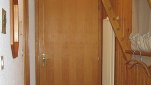 Eine Holztür mit Messinggriffen, ein Fliesenboden und eine Holztreppe mit weißer Geländer.