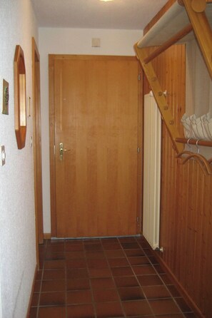 A wooden door with a brass handle, a tiled floor, and a wooden staircase with a white railing. - Résid. Monteilly B16, (Champery), by Interhome (Champery)