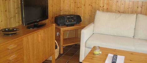 Ett rum med träpanel på väggarna, ett tv-appar, en radio, en vit soffa och ett litet bord med en fjärrkontroll.