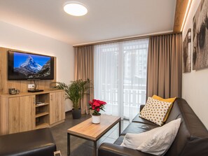 Ein modernes Wohnzimmer mit Fernseher, Holzschrank, Topfpflanze, Couchtisch und Ledersofa mit Zierkissen.