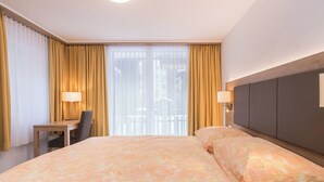 Quarto de hotel com cama, escrivaninha, cadeira, duas luminárias e vista pela janela com cortinas.