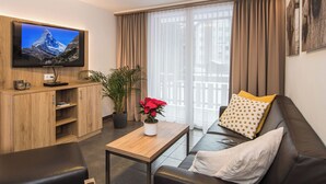 Uma sala de estar moderna com uma televisão de tela plana, um armário de madeira, uma mesa de centro com uma planta em vaso, um sofá de couro com almofadas estampadas e uma janela grande com cortinas.