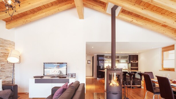 Una sala de estar moderna con chimenea, techo de madera y un comedor con sillas.