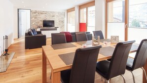 A modern living room with a wooden dining table, black chairs, a sofa, and a TV against a stone wall. - Chalet Nepomuk, (Zermatt), 1632.00 by Interhome (Zermatt)
