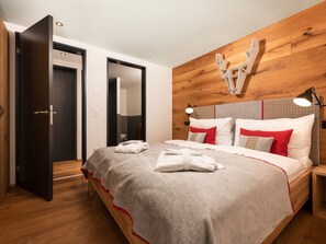 Quarto de hotel com cabeceira de madeira, cama com roupa de cama branca e vermelha, luminária de cabeceira e chão de madeira.