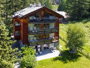 A multi-story wooden cabin with balconies, surrounded by lush greenery. - Chalet Altesse, (Zermatt), 1054.01 by Interhome (Zermatt)