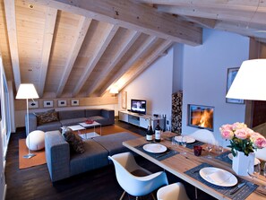 Ein modernes Wohnzimmer mit hohen Decken, einem Fernseher, einem Kamin und einer Essgelegenheit, die für eine Mahlzeit gedeckt ist.