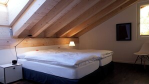 Una camera da letto con soffitto in legno, un letto, un comodino, una lampada, una sedia e una finestra.