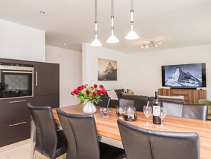 Eine moderne Küche mit Backofen, einem Esstisch mit Stühlen, einer Vase mit roten Blumen und einem Flachbildfernseher an der Wand.