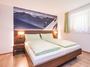 Ein Schlafzimmer mit einem großen Bett, einem hölzernen Kopfteil, zwei Nachttischen mit Lampen und einer Wandmalerei von einer Berglandschaft.