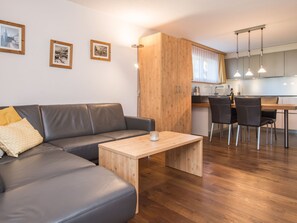 A modern living room with a grey leather sofa, a wooden coffee table, and a dining area with a kitchen in the background. - Haus Felice, (Zermatt), 1333.00 by Interhome (Zermatt)