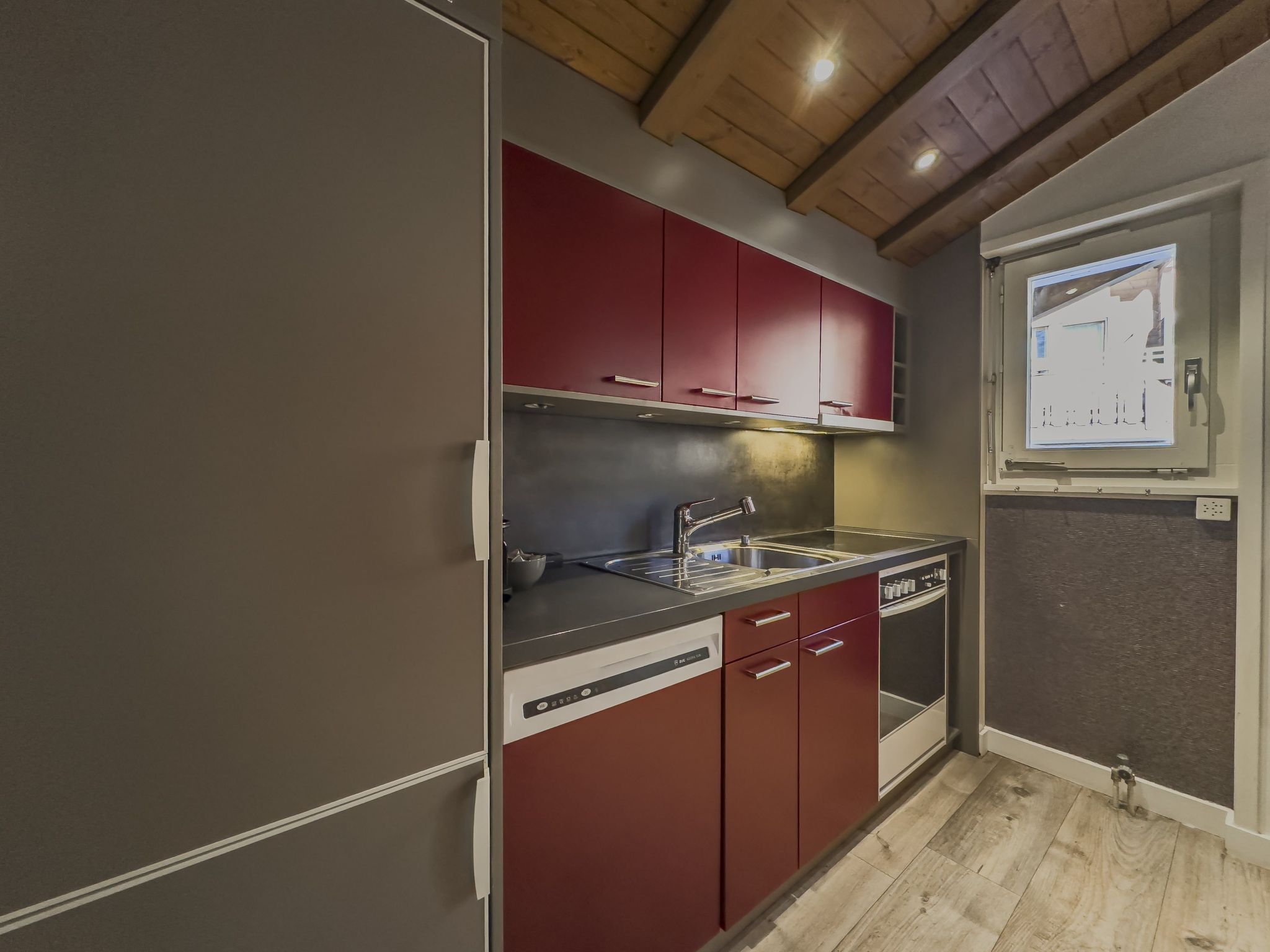 Une cuisine compacte avec des meubles de rangement rouges, un évier en acier inoxydable et un four encastré.
