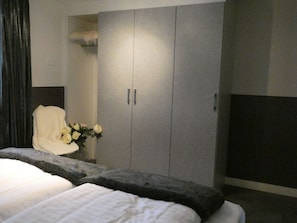 A hotel room with a bed, a grey wardrobe, a white chair, and a vase with flowers. - Haus Venus, (Zermatt), by Interhome (Zermatt)
