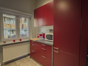 A kitchen with red cabinets, a window with a view of buildings, a radiator, and a microwave on the counter. - Haus Venus, (Zermatt), by Interhome (Zermatt)