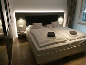 A double bed with two pillows, a nightstand with a magazine, and a wall-mounted light. - Haus Venus, (Zermatt), by Interhome (Zermatt)