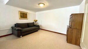 Una habitación con un sofá gris, un cuadro en la pared, un jarrón con girasoles y un mueble de madera.