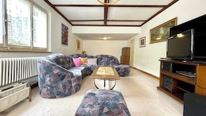 Sala de estar con sofá seccional, reposapiés y televisor sobre un mueble de madera.