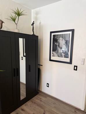 Ett rum med en svart garderob, en inramad tavla på väggen och en krukväxt placerad ovanpå garderoben.