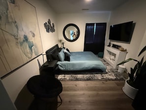 Ein modernes Schlafzimmer mit einem Bett, einem runden Spiegel, einem Fernseher und einem großen abstrakten Gemälde.