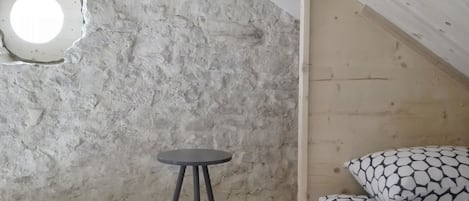 A room with a concrete wall, a small round table, and a bed with patterned pillows.