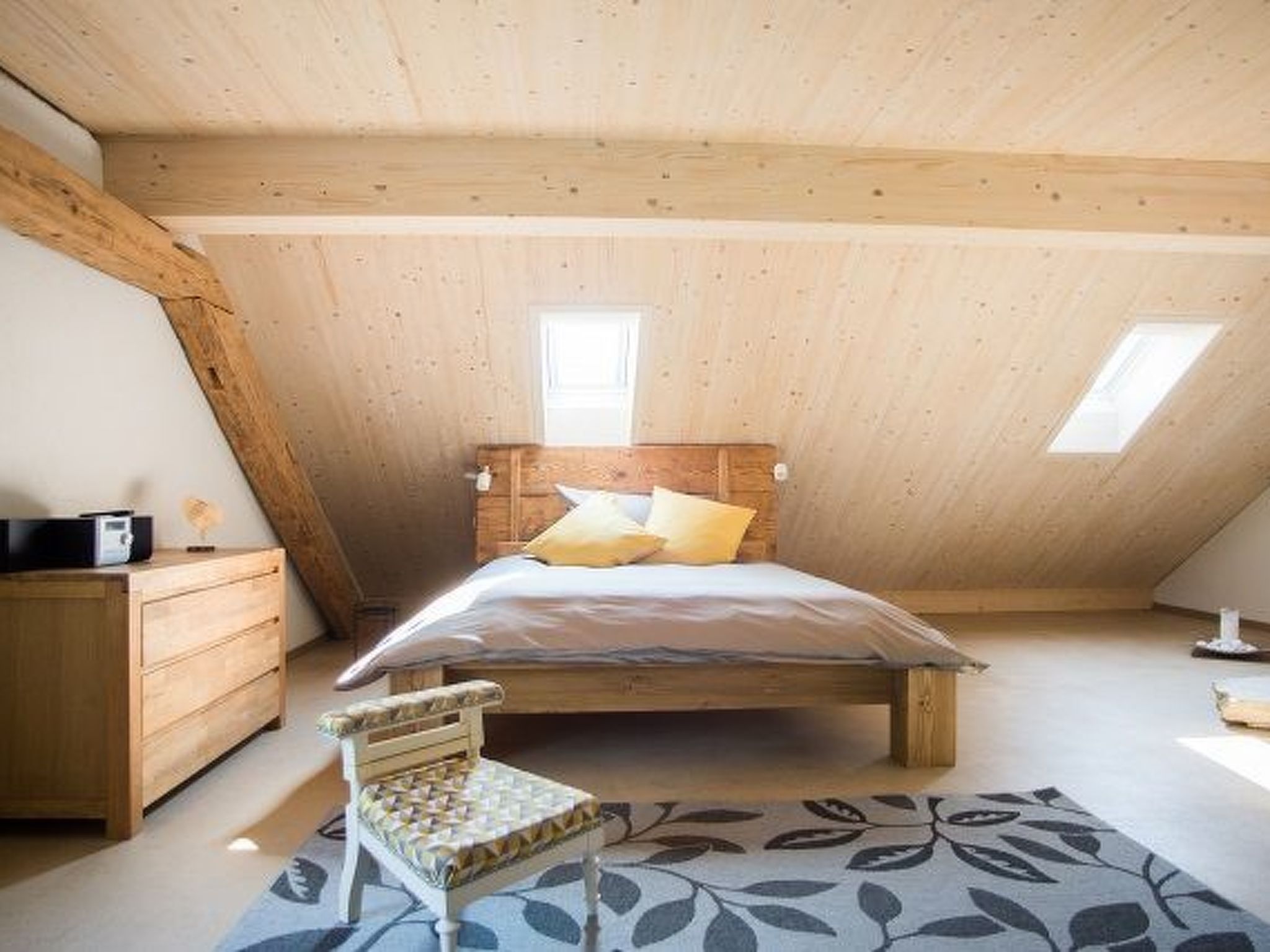 A bedroom with a sloped ceiling, a bed, a dresser, a chair, and a window.