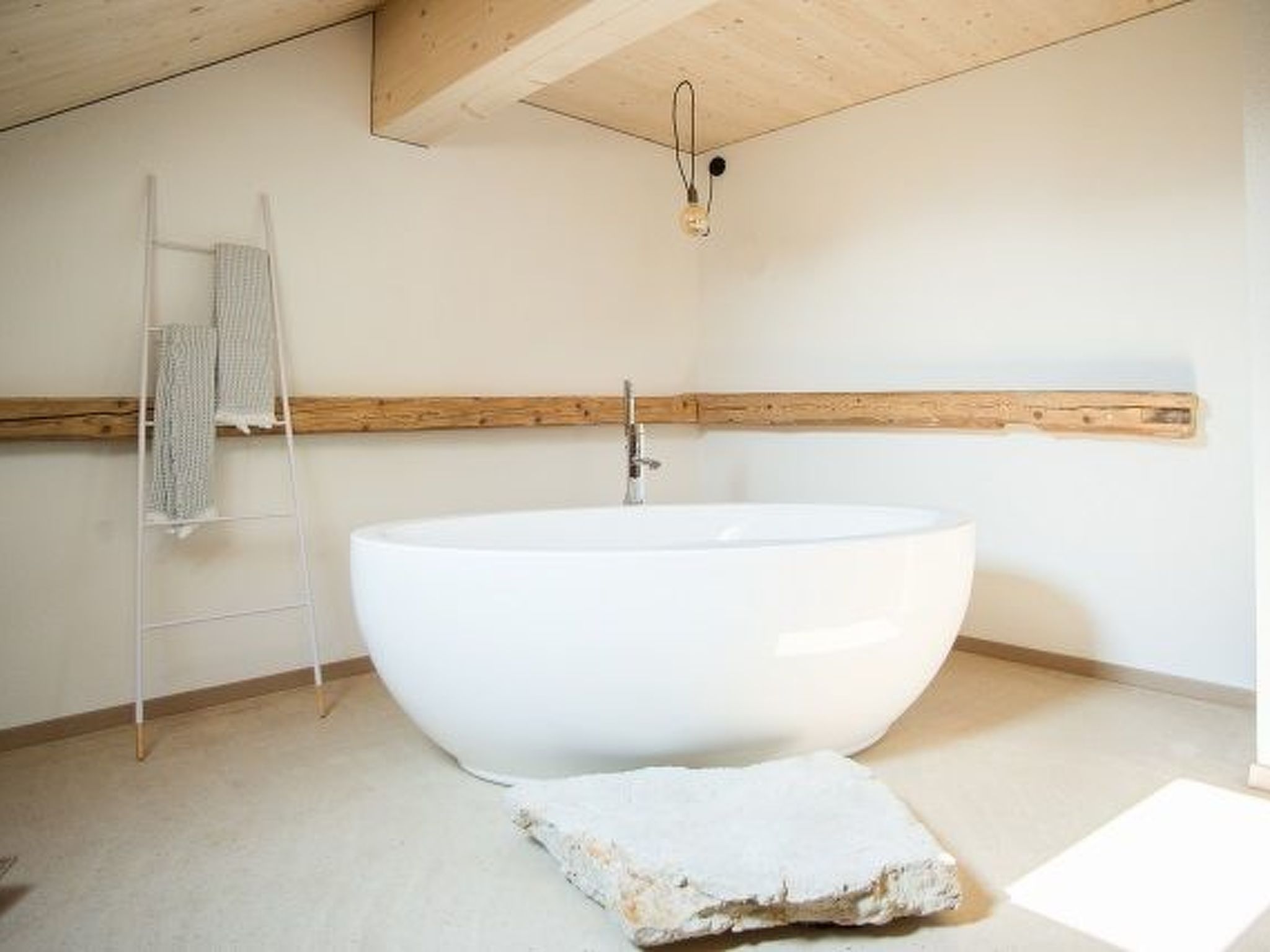 Un baño moderno con una bañera independiente grande, un perchero y un techo con vigas de madera.