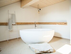 Un baño moderno con una bañera independiente grande, un perchero y un techo con vigas de madera.
