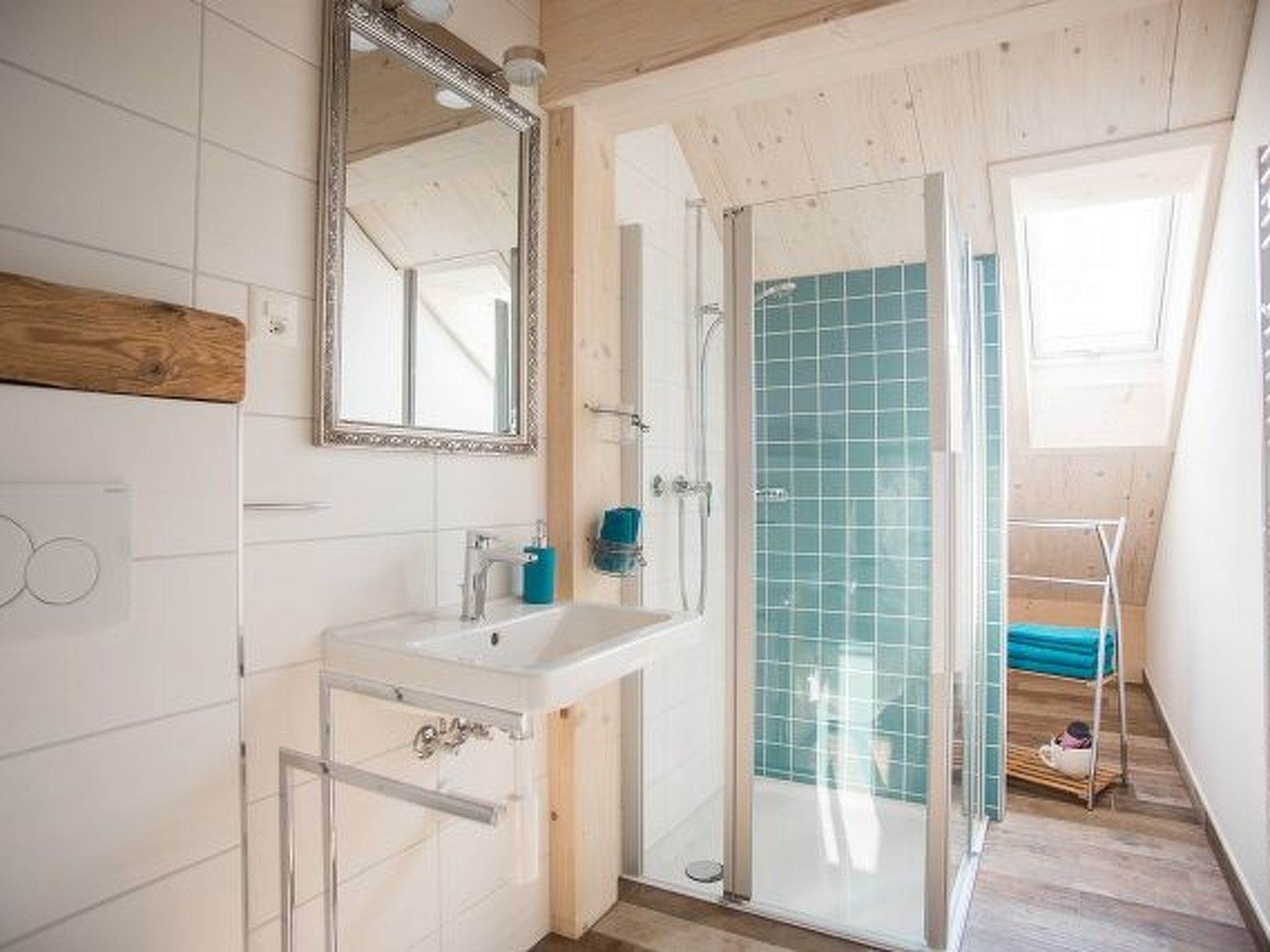 Un baño con lavamanos blanco, espejo, cabina de ducha de vidrio y suelo de madera.