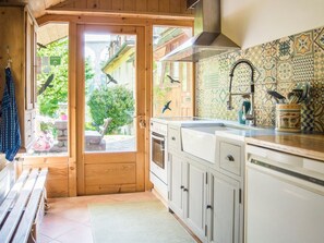 Een keuken met houten kastjes, een roestvrijstalen spoelbak en uitzicht op de tuin via een glazen deur.