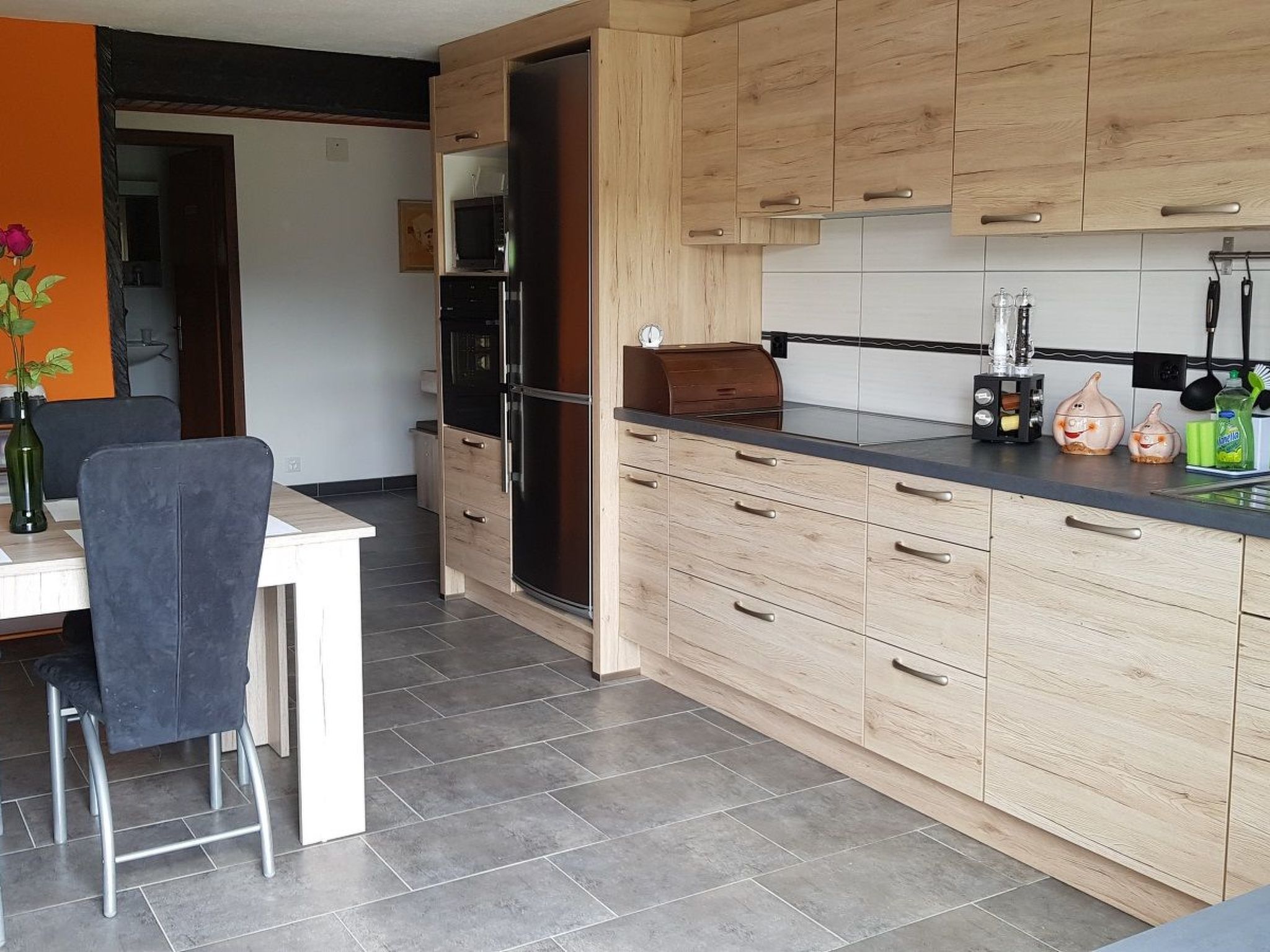 Cozinha moderna com armários de madeira, bancada preta e área de refeições com uma cadeira e mesa.