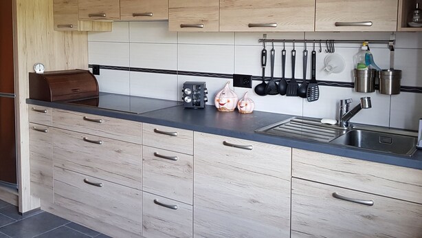 A modern kitchen with wooden cabinets, a black countertop, and various kitchen utensils hanging above the sink. - Appartement - Sous les Barres, (Montfaucon), by Interhome (Montfaucon)