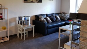 A living room with a dark blue sofa, patterned cushions, a small white table, and a bookshelf. - Appartement - Sous les Barres, (Montfaucon), by Interhome (Montfaucon)