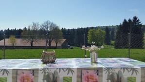 An outdoor table with a floral tablecloth, a decorative basket, and a vase with flowers. - Appartement - Sous les Barres, (Montfaucon), by Interhome (Montfaucon)