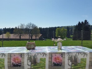 Et udendørs bord med et blomstret borddække, en flettet kurv og en vase med blomster.