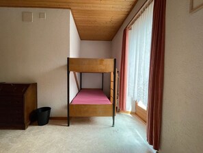 Camera con letto a castello, soffitto in legno, finestra con tende e una piccola scrivania.