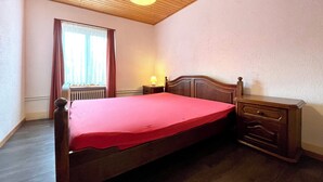 Un dormitorio con techo de madera, una cama con colcha roja, una mesita de noche con lámpara y un aparador.