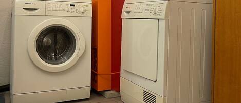 A laundry room with two white washing machines and a red water heater.