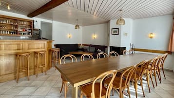 Un comedor amplio con una larga mesa de madera y sillas a juego, una zona de bar con taburetes y un rincón de estar acogedor con un sofá y cojines.